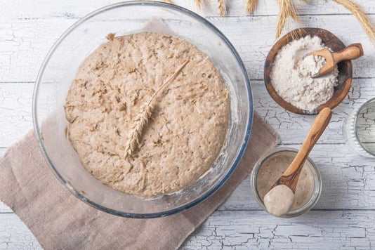 Une pâte à pain en train de poser et à côté la farine et le levain qui ont servi à sa fabrication