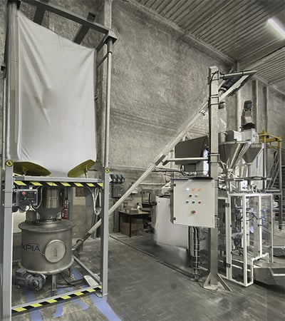 Atelier de conditionnement de établissement Michel Côme avec au premier plan une videuse bigbag en train de décharger de la farine via une vis flexible vers l'ensacheuse verticale