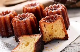 Une assiette de cannelés dont un coupé en deux laisse apparaître le cœur moëlleux