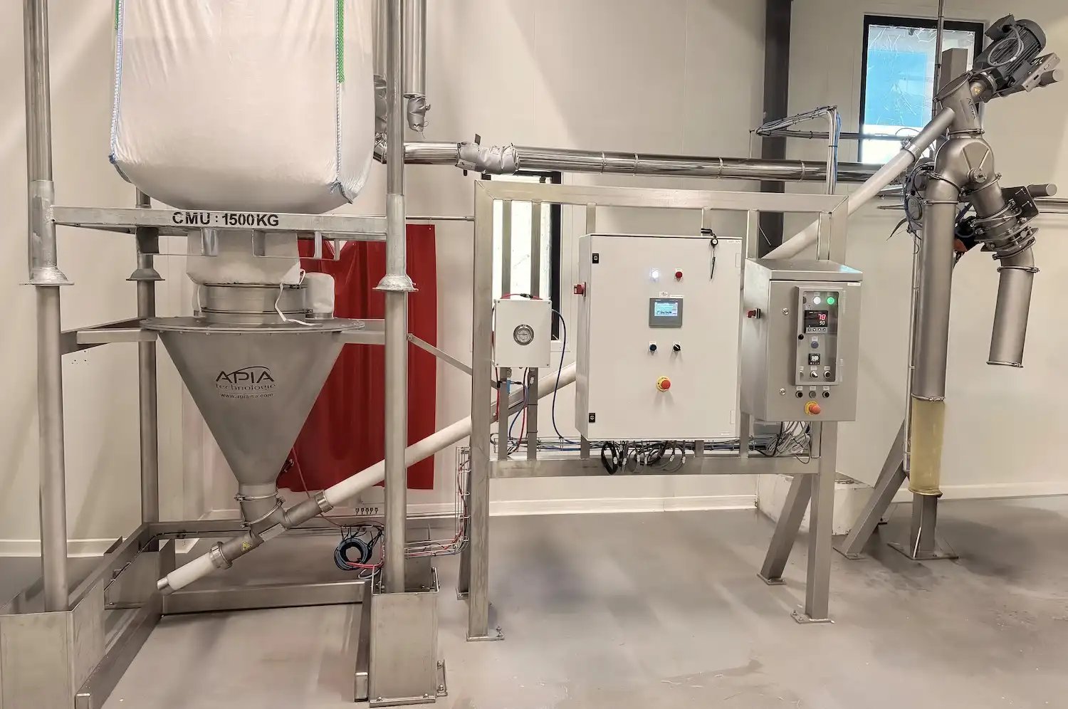Installation APIA Technologie chez Confiserie du Roy René avec une videuse big-bags et sa trémie tampon sous laquelle une vis de transfert automatique convoie les amandes émondées jusqu'aux conduits desservant alternativement un remplissage de bac Europe ou l'échaudoire