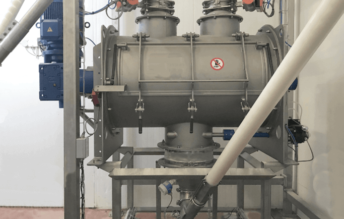 En aval d'un mélangeur industriel d'ingrédients alimentaires secs, un transfert automatique par vis flexible alimente une ensacheuse