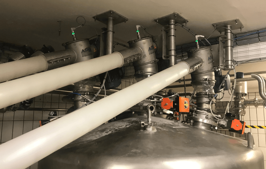 Plusieurs tubes de transfert d'ingrédients dosent une recette dans une cuve de préparation alimentaire industrielle